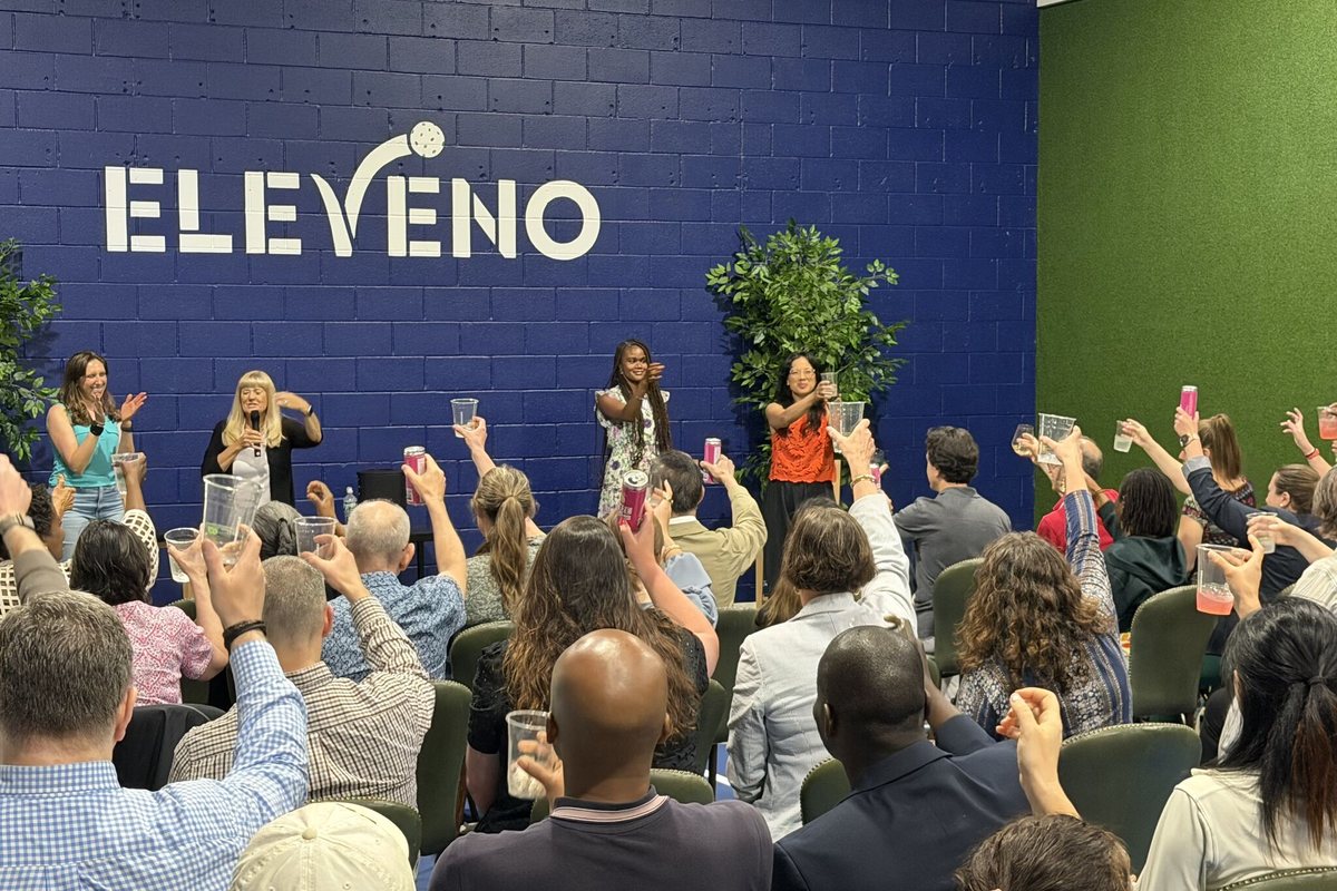 A room of guests raising a toast in front of the ELEVENO wall