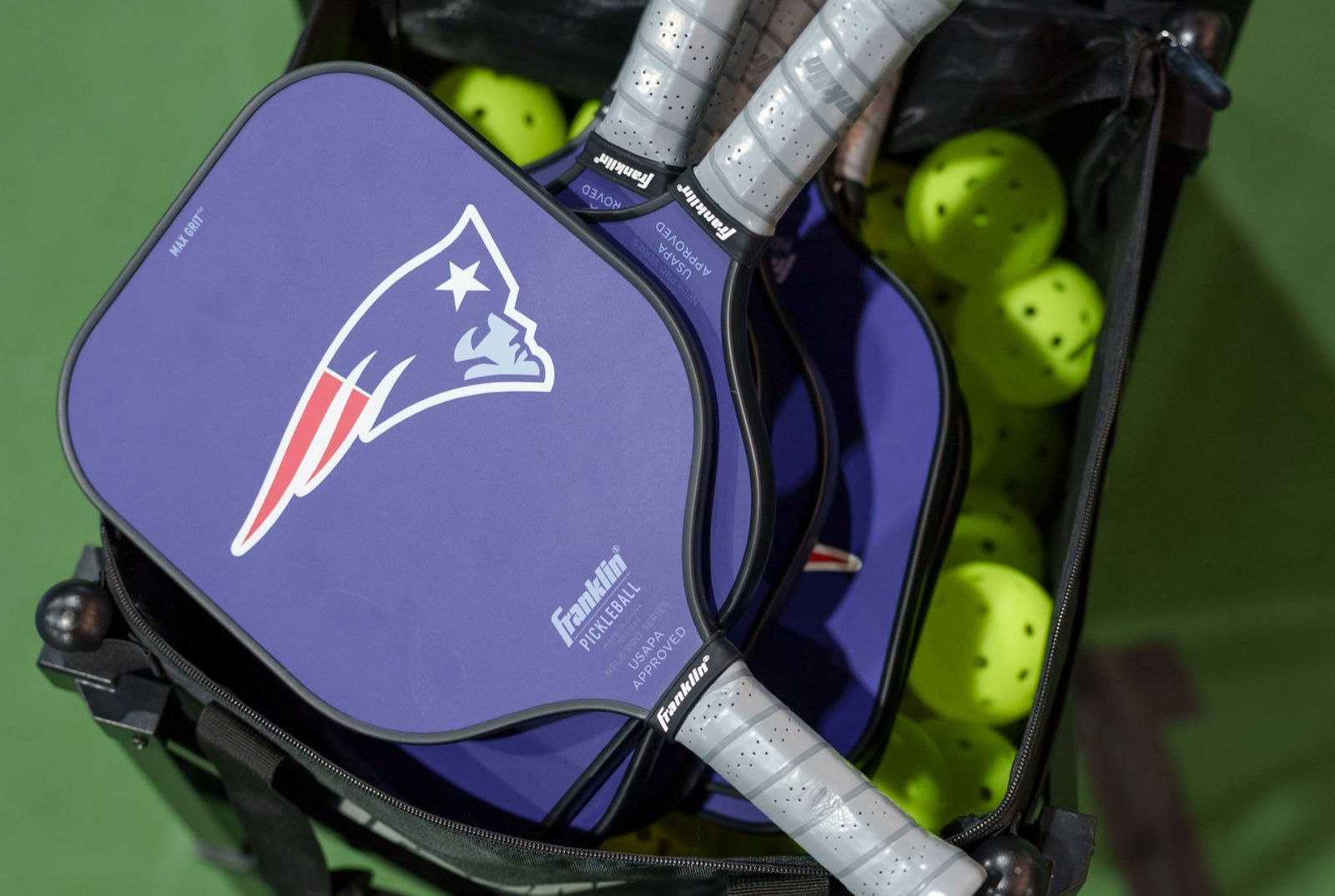 A Patriots-branded paddle resting in a basket of balls courtside